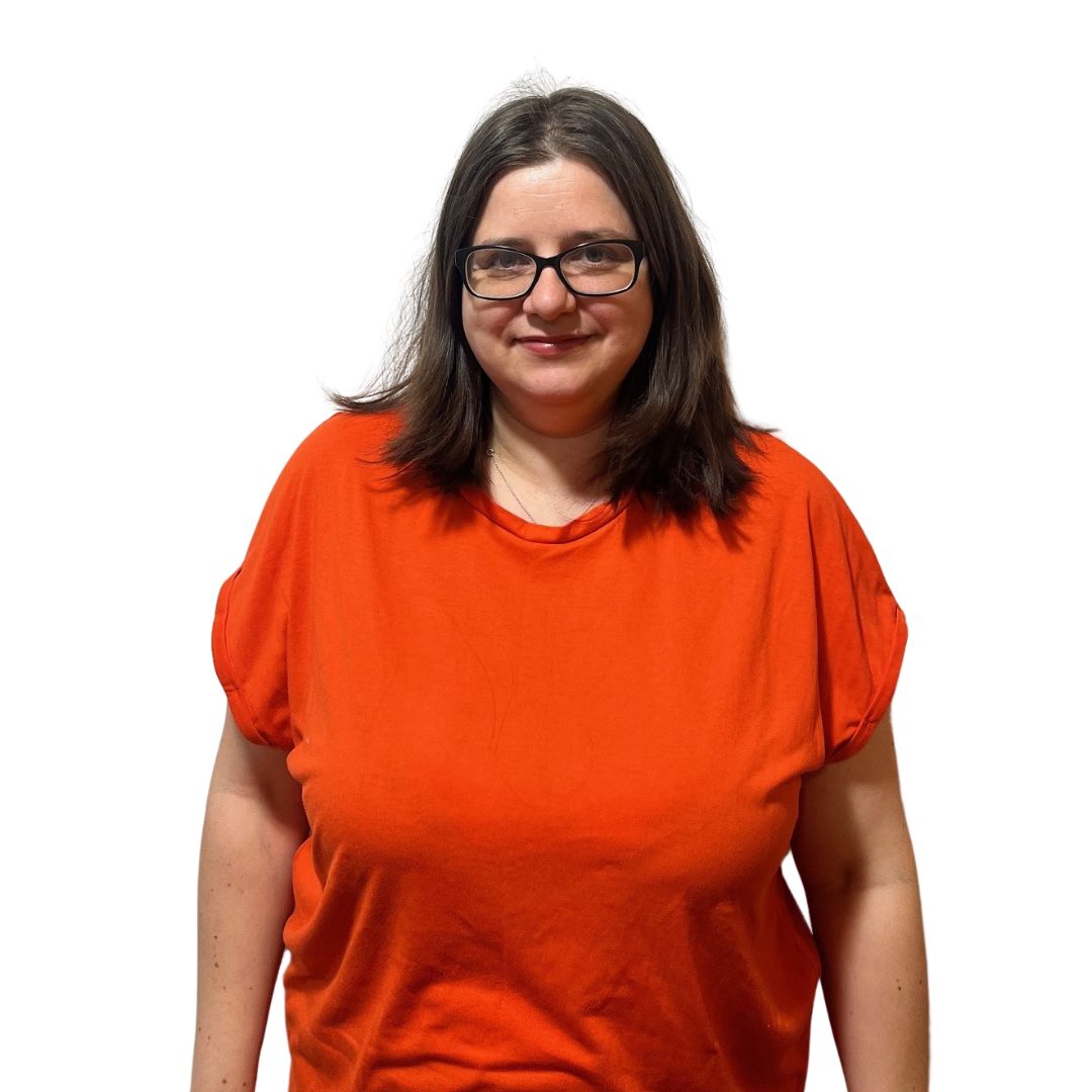 Our FYPO, Vicky, smiles at the camera. She has long, chestnut brown hair and is wearing black framed glasses and a bright red top with white flowers on it.